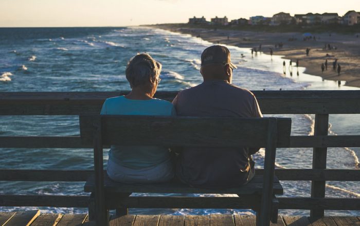 Älteres Eherpaar sitzt auf Pier und schaut aufs Meer