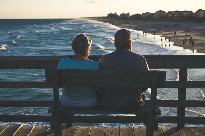 Älteres Eherpaar sitzt auf Pier und schaut aufs Meer